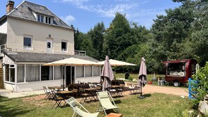 Een huis met een patio, meubilair en parasols, een rode foodtruck en een gazon.