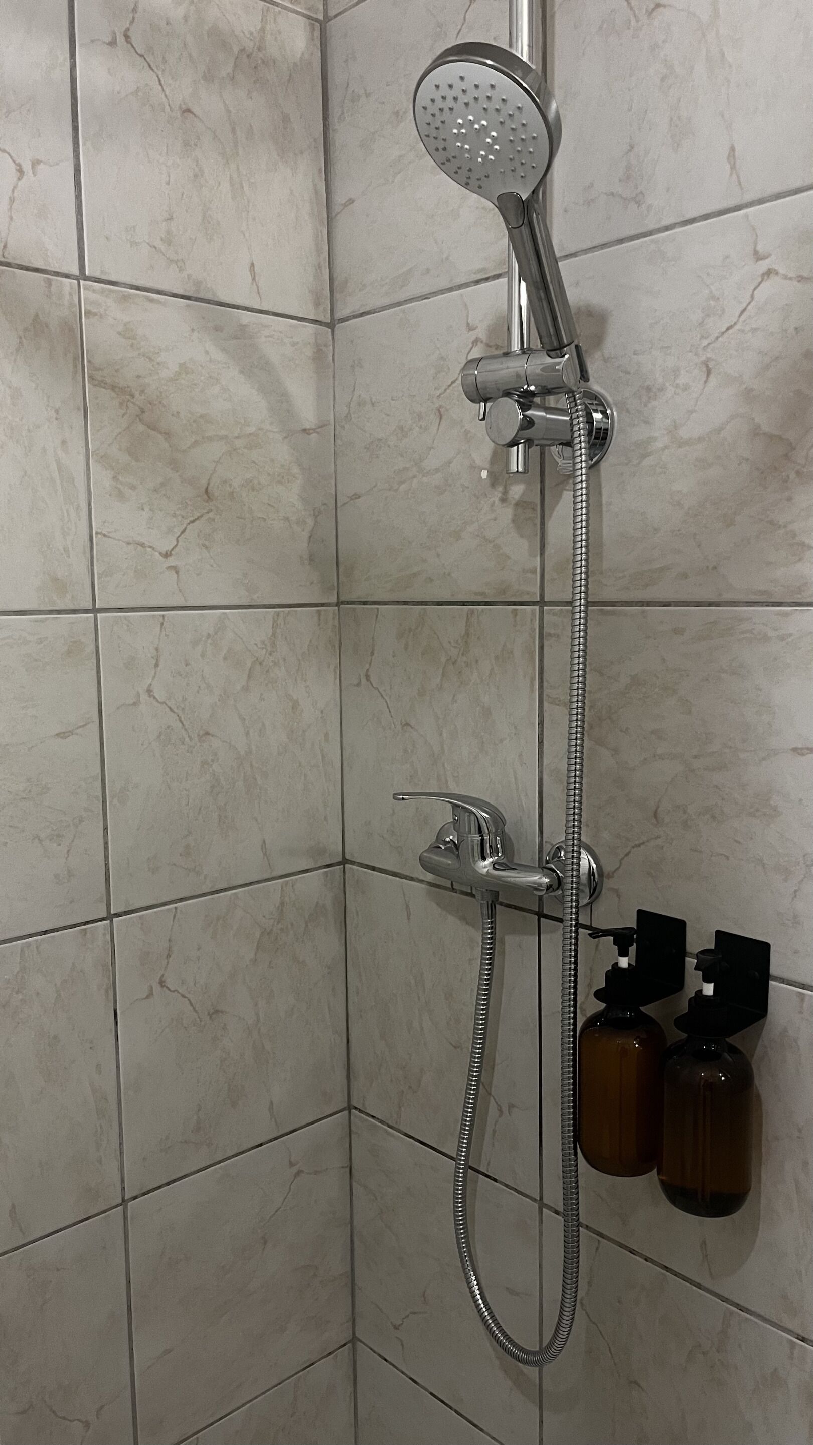 A shower with a handheld showerhead, a wall-mounted faucet, and a handheld shower attachment.