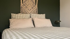 Een bed met een geruit beddegoed, twee kussens en een macramé wanddecoratie.