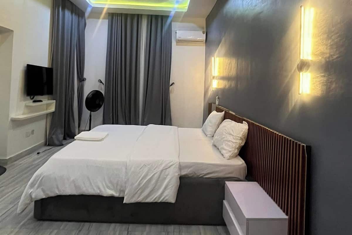 A modern hotel room with a large bed, a bedside table, a TV, and a ceiling light fixture.