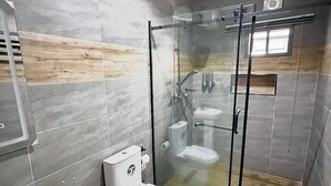 A modern bathroom with a glass-enclosed shower, a toilet, and a sink. - Smridu Hotel (Lagos)