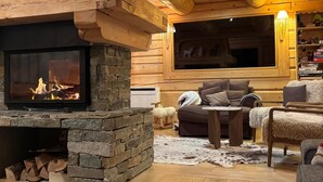 L’intérieur d’un chalet confortable, avec une cheminée en pierre, des murs en bois, un coin salon accueillant et une grande fenêtre.