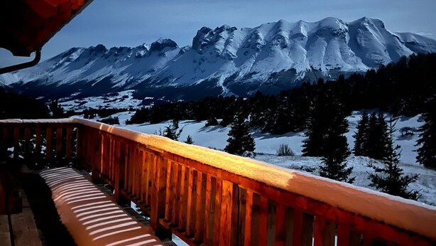 Une terrasse en bois dotée d’une rambarde, d’où l’on peut admirer une chaîne de montagnes enneigées.
