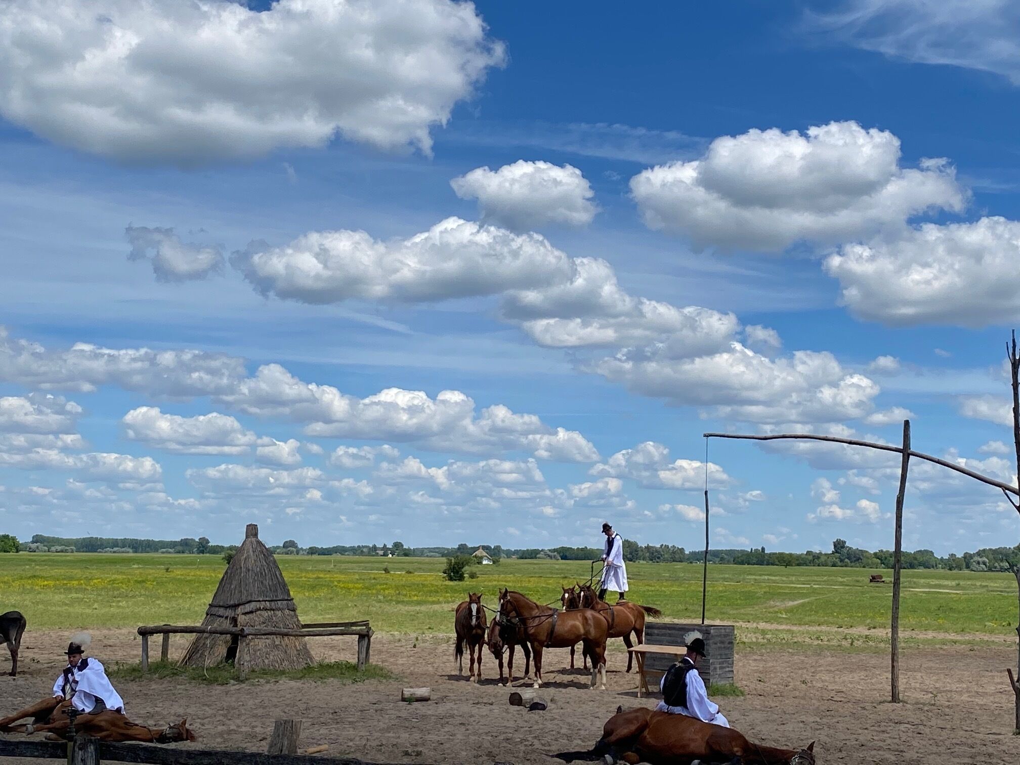 A rural scene with a thatched-roof structure, horses, and people in traditional attire.