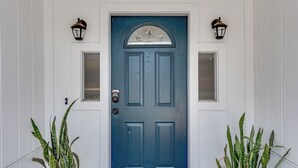 A blue door with two small windows and a decorative glass panel above it. There are two wall-mounted lanterns on either side of the door. - Stylish Retreat Near Beaches & Attractions - Private, Clean, Comfortable (Jacksonville)