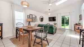 A spacious living room with a dining area, a green sofa, a ceiling fan, and a TV mounted on the wall. - Stylish Retreat Near Beaches & Attractions - Private, Clean, Comfortable (Jacksonville)