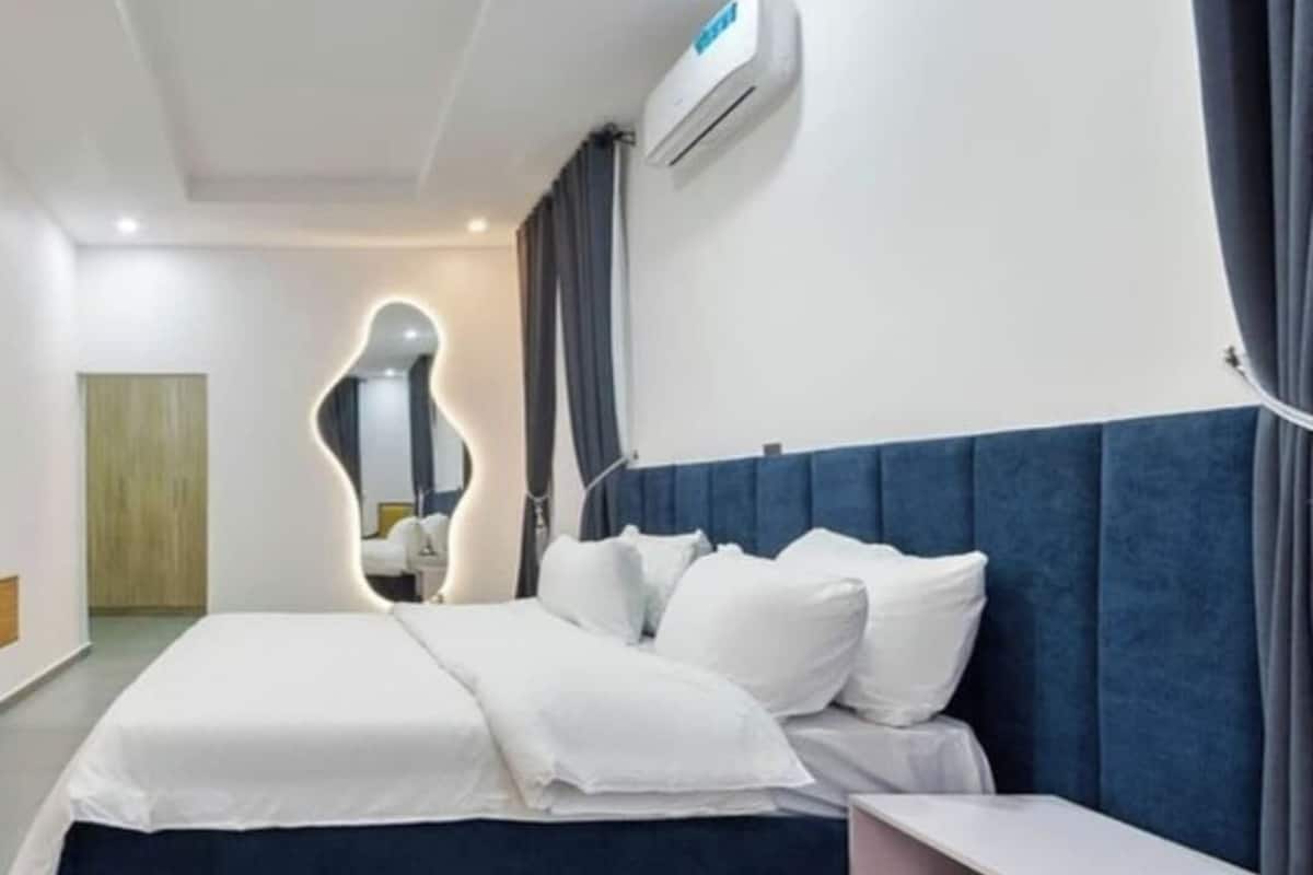 A modern hotel room with a large bed, a bedside table, and a built-in air conditioning unit.