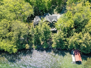 Une vue aérienne d’une maison entourée d’une forêt dense et bordée d’un plan d’eau.