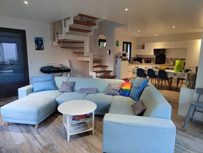 A modern living room with a light blue sectional sofa, a white coffee table, and a staircase with wooden steps. - New house on Oléron, 10 minutes from the beach (Le Grand-Village-Plage)