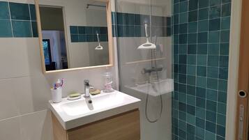 Een moderne badkamer met een witte wastafel, houten kastjes, een glazen douchecabine en teal-gekleurde wandtegels.