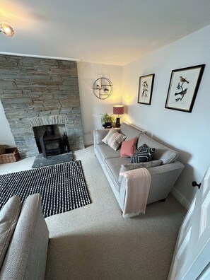 A cozy living room with a stone fireplace, a grey sofa with cushions, a patterned rug, and framed artwork on the wall. - Gorge View Welsh Slate Cottage (Cilgerran)