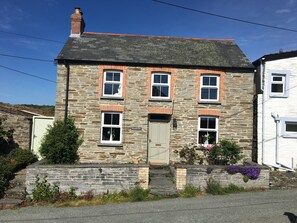 A stone house with a tiled roof, a front door, and a small porch with flowers. - Gorge View Welsh Slate Cottage (Cilgerran)