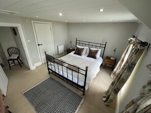 A bedroom with a bed, a chair, a nightstand, a radiator, and a window with curtains. - Gorge View Welsh Slate Cottage (Cilgerran)