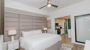 Un dormitorio moderno con una cama grande, mesitas de noche, un ventilador de techo y vistas a la cocina.