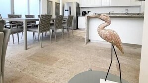Une cuisine moderne avec des meubles blancs, un coin repas avec des chaises grises et une sculpture d’oiseau décorative posée sur une table.