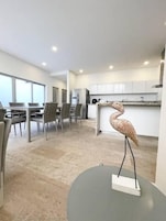 Una cocina moderna con armarios blancos, un comedor con sillas grises y una escultura decorativa de pájaro sobre una mesa.
