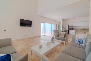 Amplia sala de estar con televisor de pantalla plana, un comedor y una cocina al fondo.