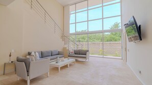 Un salon spacieux avec une grande fenêtre, un canapé, une table basse et un téléviseur fixé au mur.