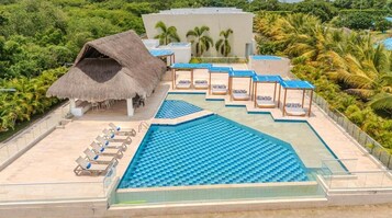 Una piscina en la azotea con baldosas azules, sillas de descanso y una estructura con techo de paja.