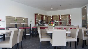 Een modern restaurant met hoge tafels en zitjes, een bar en een zichtbare keuken op de achtergrond.