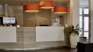 Een receptiegedeelte met een modern design, met een receptiebalie, drie hanglampen en een bord met een welkomstboodschap aan de muur.
