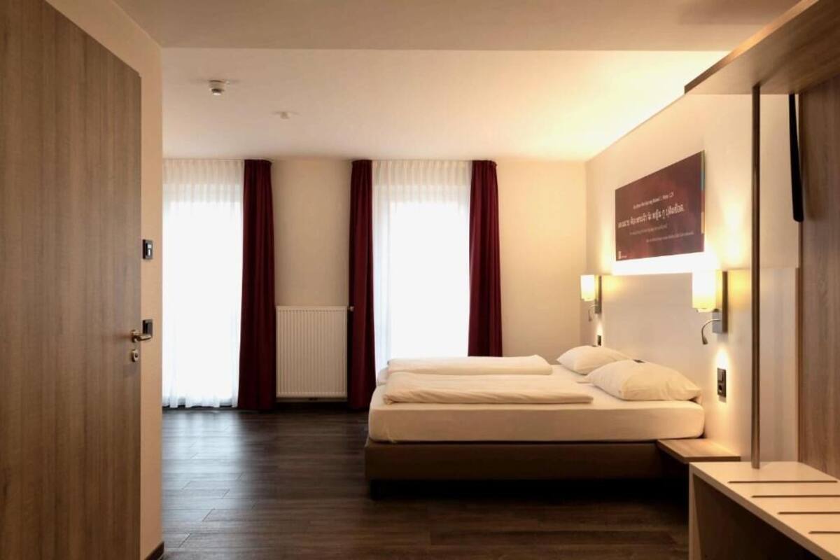 Ein Hotelzimmer mit Bett, Nachttischen, einer Wandleuchte und einem Vorhangfenster.