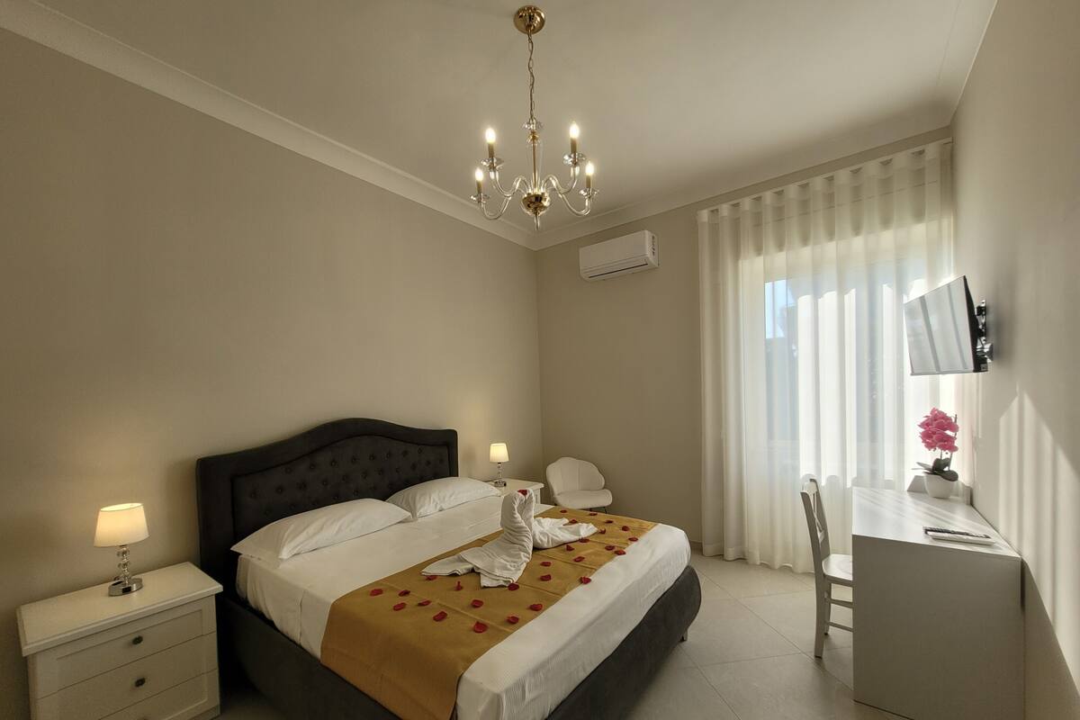 Ein Hotelzimmer mit Bett, Nachttischen, Schreibtisch, Stuhl, Fernseher und einer Chandelier.