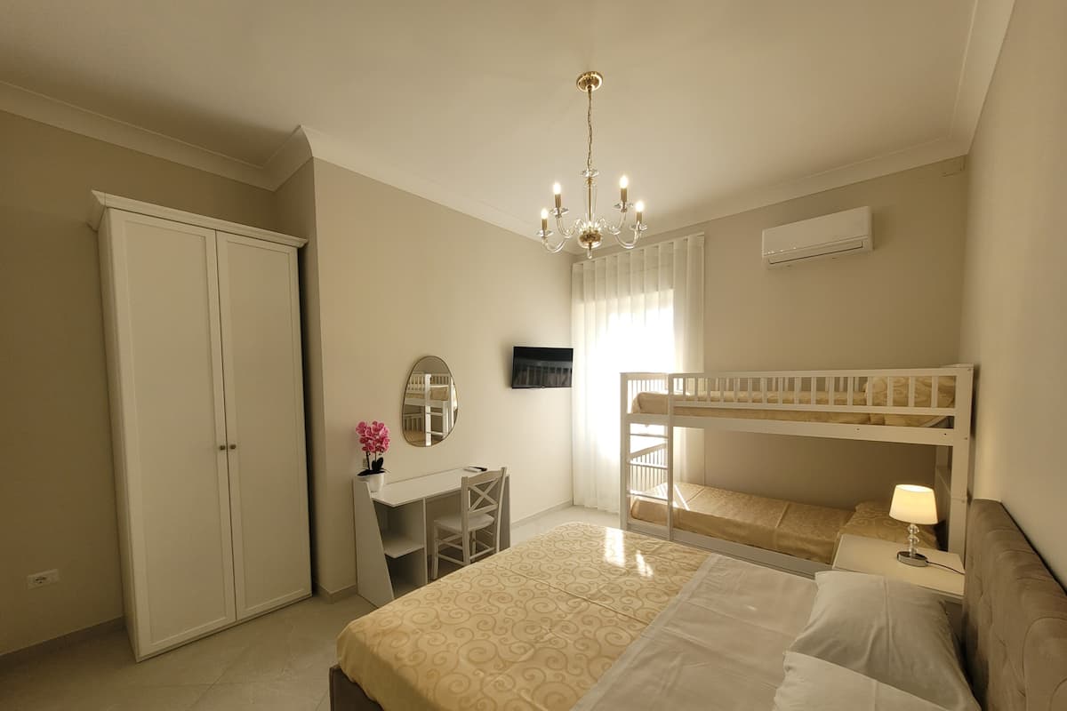 Ein Schlafzimmer mit Etagenbett, Schreibtisch mit Stuhl, Kleiderschrank, einer Chandelierleuchtre und einer Klimaanlage.