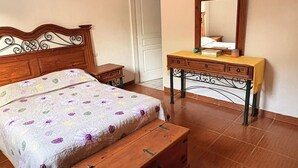 Een slaapkamer met een houten bed, nachtkastje, kapstok en een spiegel aan de muur.