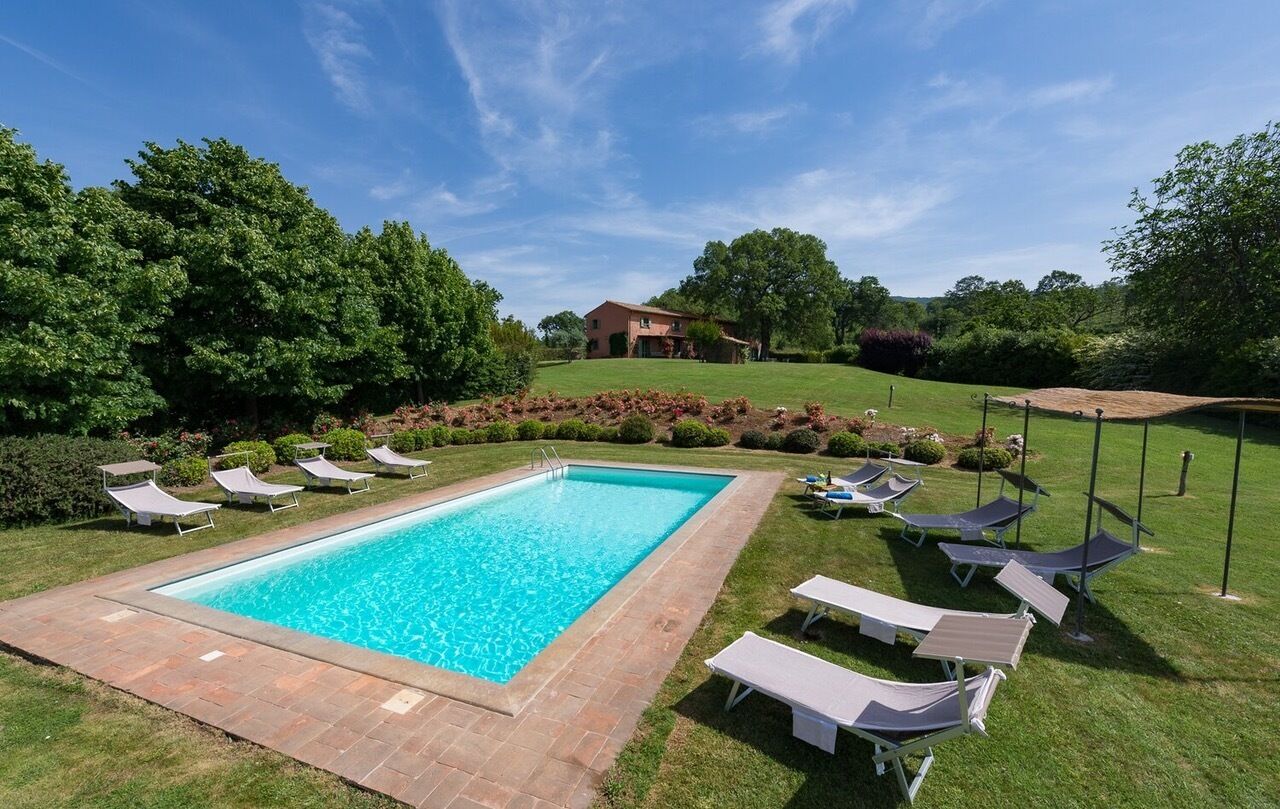 Una piscina rectangular rodeada de sillones de descanso y un césped cuidado.