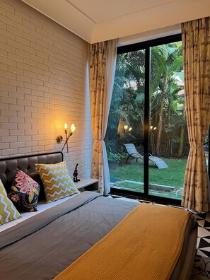 Une chambre avec un mur en briques, un lit recouvert d’une couverture jaune, deux oreillers et une table de chevet avec une lampe.