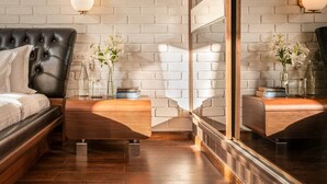 A modern bedroom with a tufted headboard bed, wooden nightstands, a large mirror, and white brick wall. - Luxury Villa Near Beach with Pvt Pool & Garden (Anjuna)