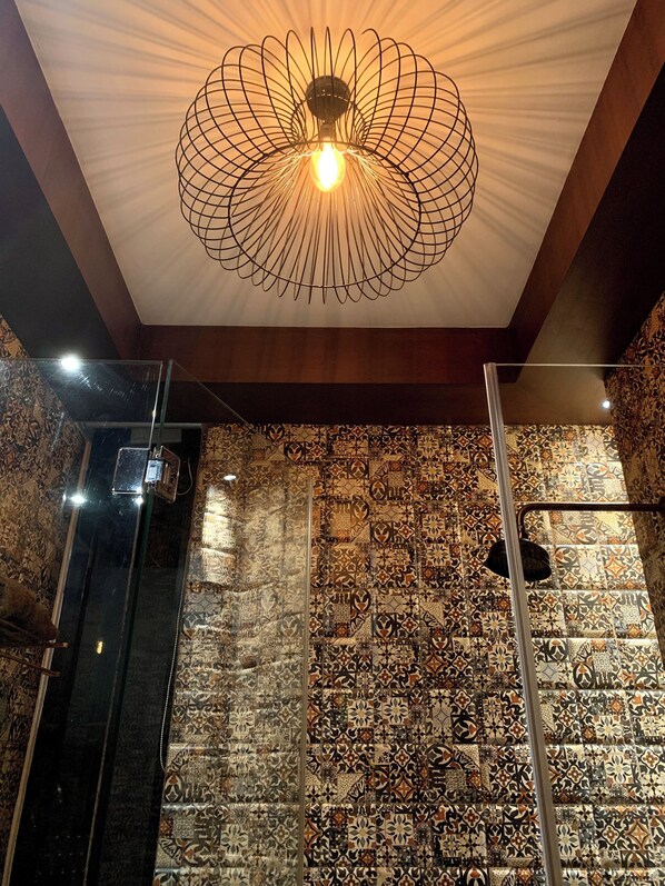 Una habitación con pared de baldosas estampadas, una lámpara moderna y un separador de vidrio.