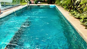 A swimming pool with clear blue water, surrounded by lush greenery and a white chair. - Luxury Villa Near Beach with Pvt Pool & Garden (Anjuna)