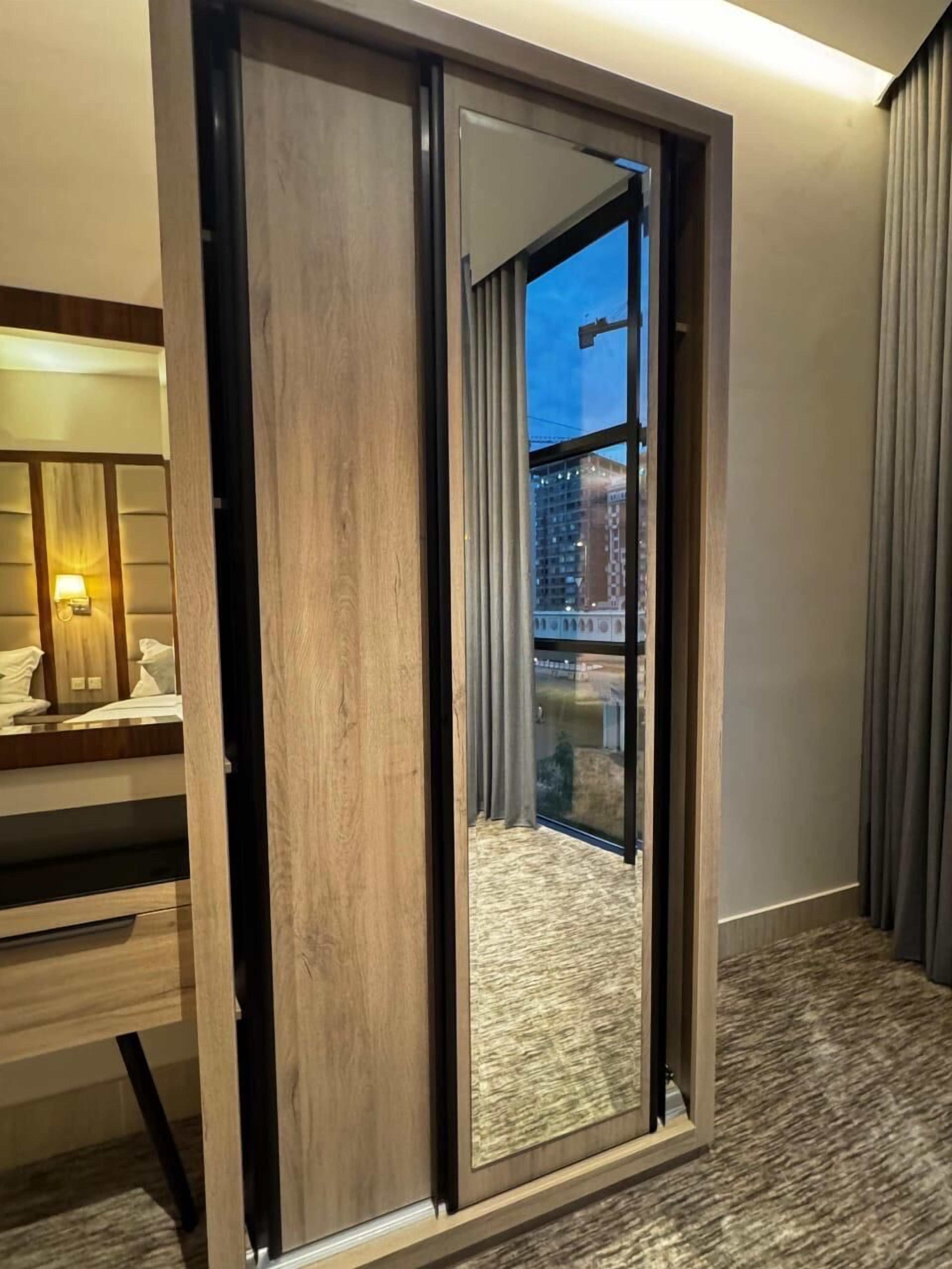 A hotel room with a sliding door leading to a balcony, a bed with a headboard, a bedside table, and a lamp.