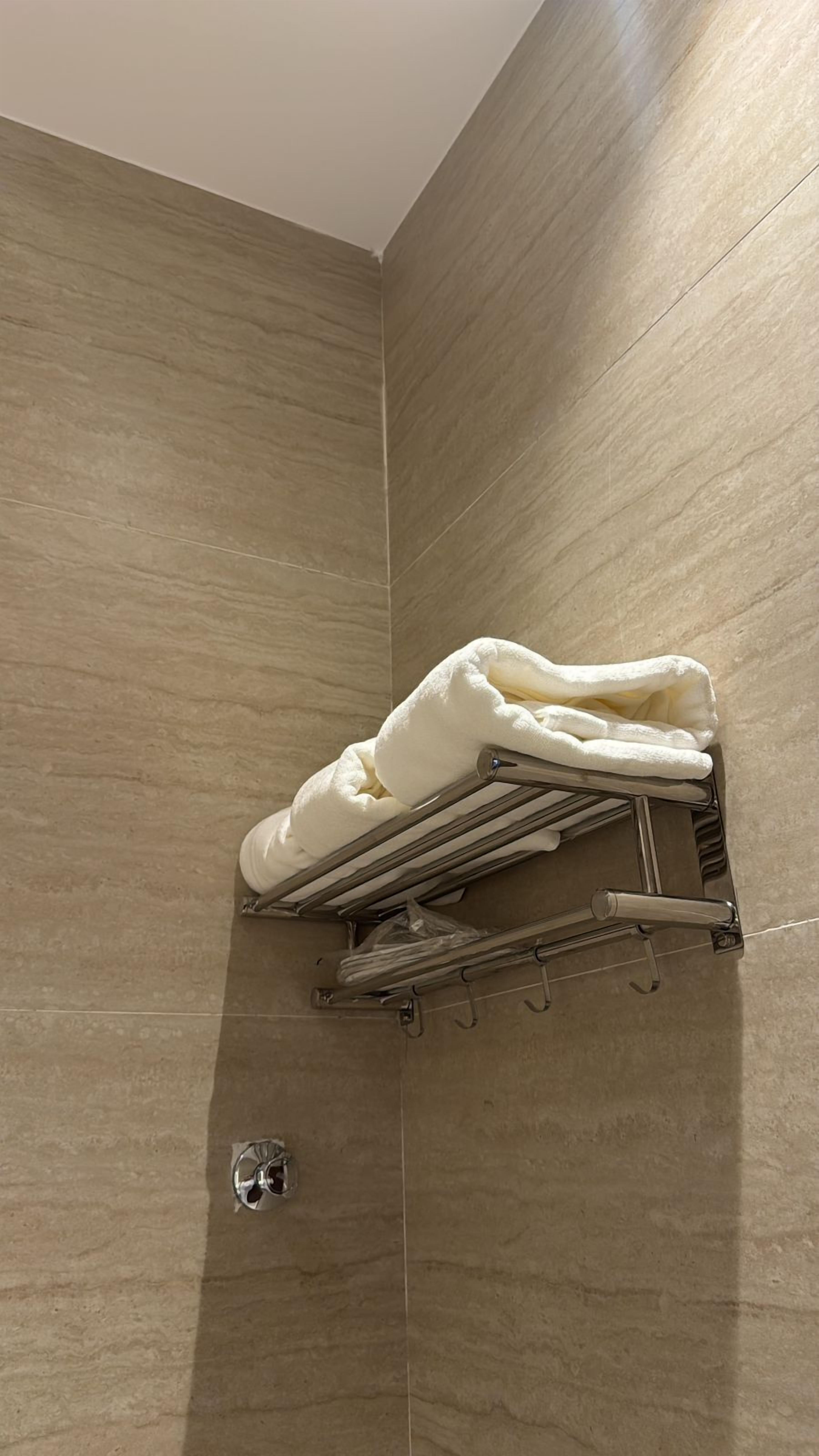 A bathroom with beige tiled walls, a towel rack with a folded towel, and a showerhead.
