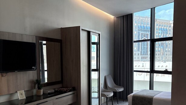 Una habitación de hotel moderna con una cama grande, un escritorio con televisión de pantalla plana, una silla y un ventanal con vistas a la ciudad.