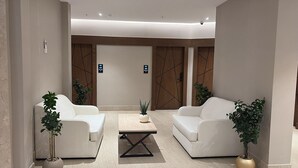 Un vestíbulo moderno con dos sofás blancos, una mesa de centro y plantas en macetas.