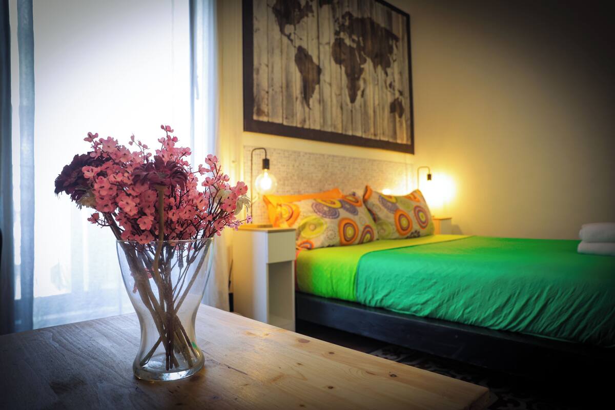A room with a bed, a nightstand, a vase with flowers, and a world map on the wall.