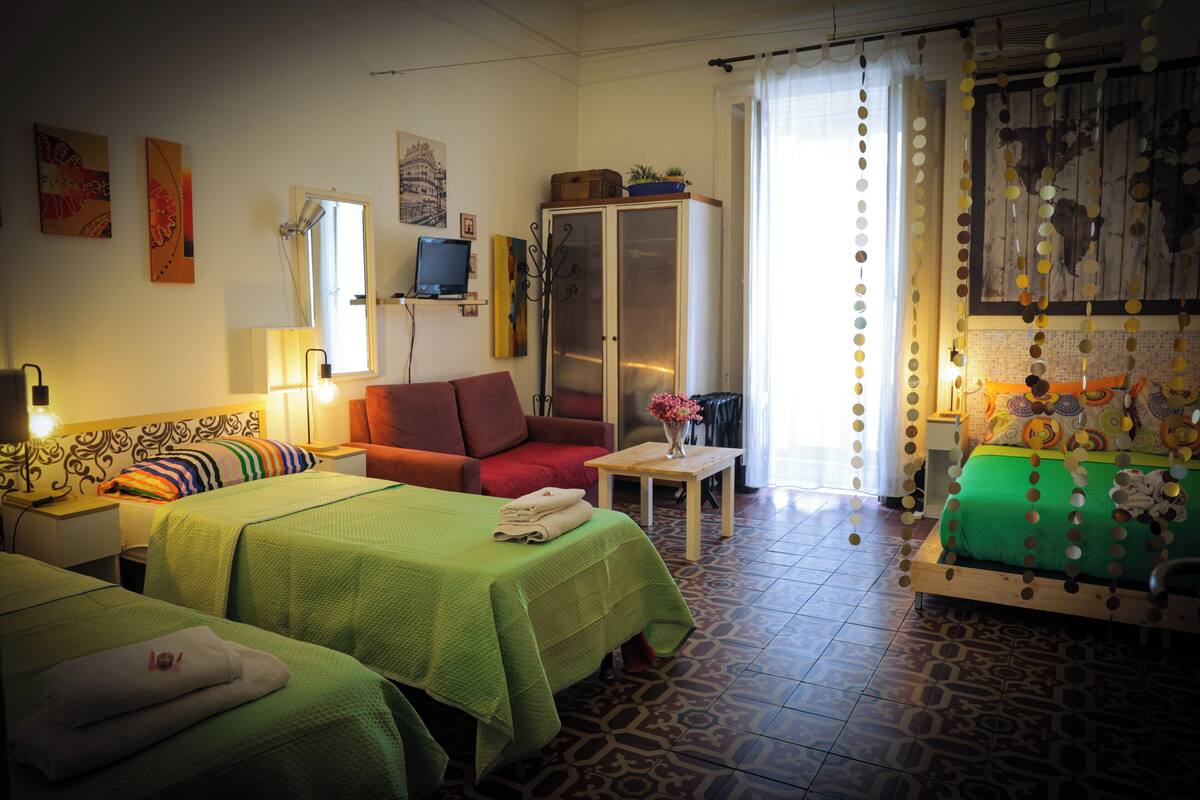 A hotel room with two beds, a sofa, a cabinet, and a television.