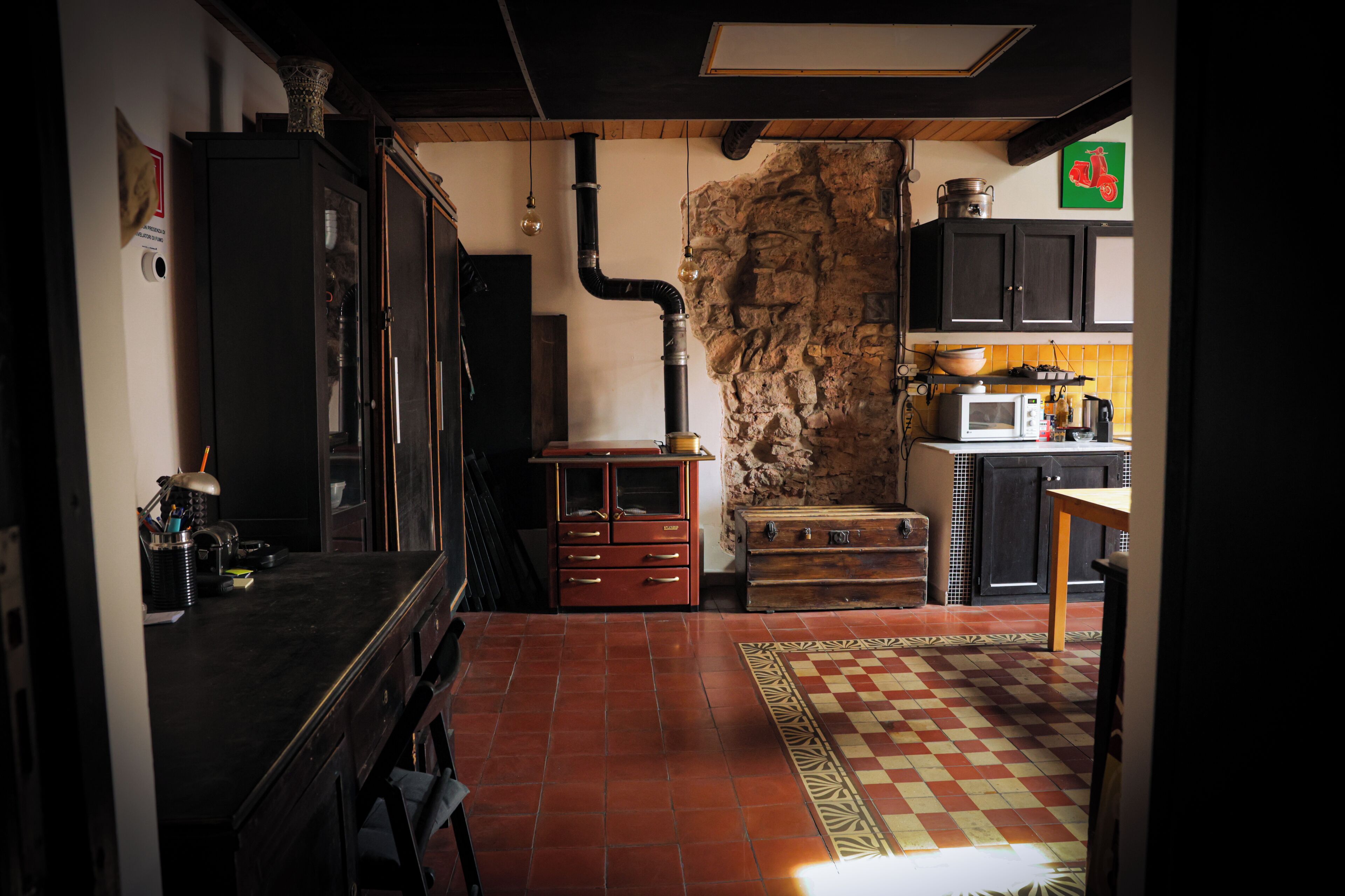 A kitchen with a stone wall, wooden cabinets, and a tiled floor.