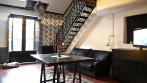 Ein gemütlicher Wohnbereich mit Treppe, einem schwarzen Ledersofa, einem Holztisch und einem Fernseher auf einem Schrank.