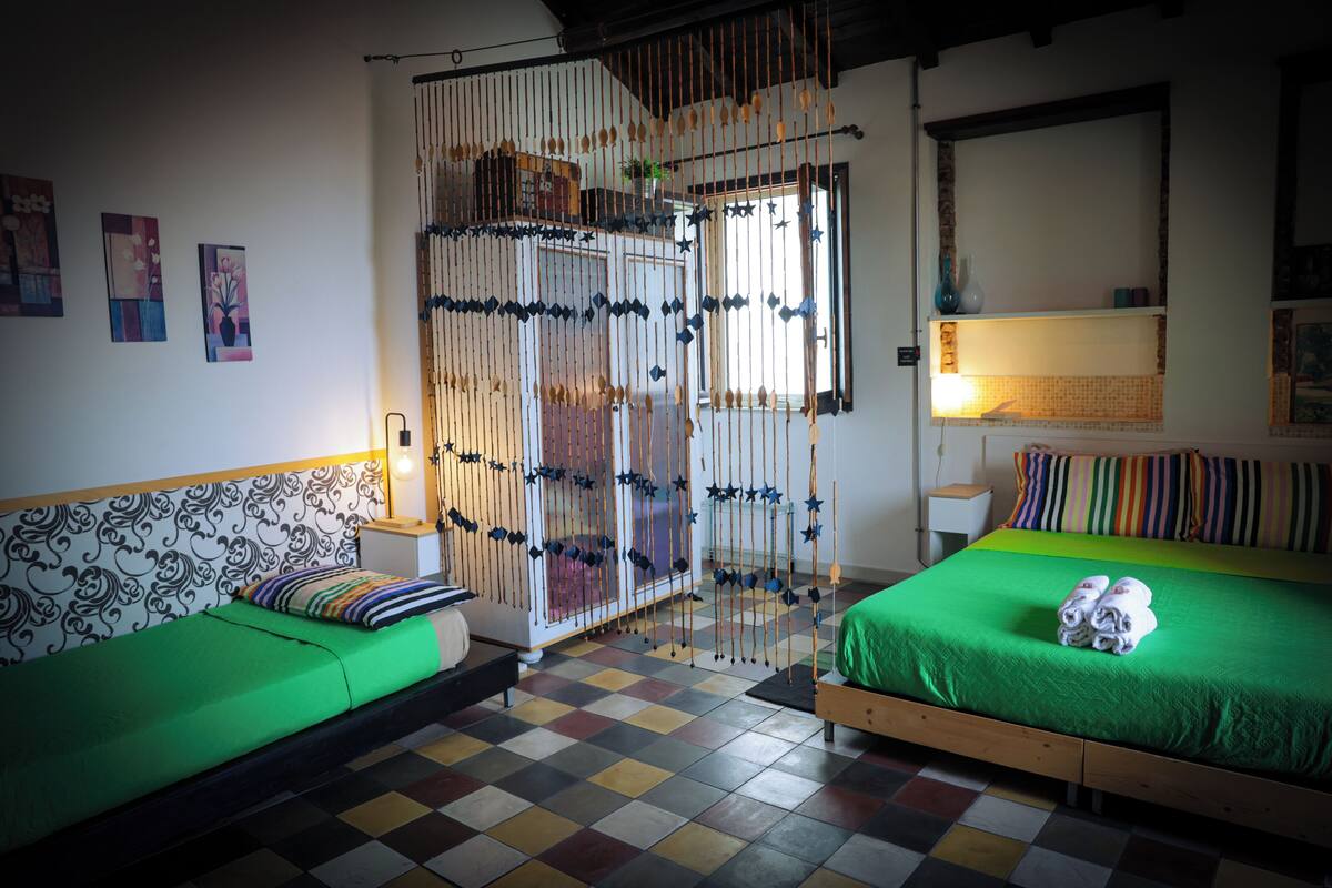 A room with a checkered floor, a green sofa, a bed with a green bedspread, and a decorative wooden partition.