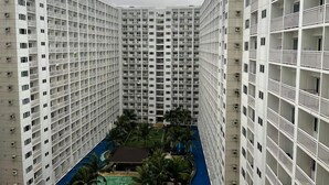 Un edificio alto con numerosi piani, balconi e un cortile centrale con piscina e palme.