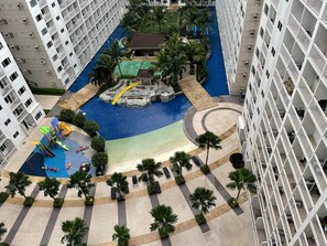 Um hotel moderno com piscina central, área de recreação infantil e um pátio ajardinado com palmeiras.