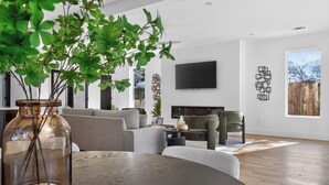 Ein modernes Wohnzimmer mit einer Couch, Sesseln, einem Couchtisch und einem an der Wand montierten Fernseher.