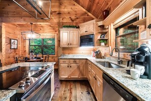 A wooden cabin kitchen with granite countertops, a built-in stove, a microwave, and a coffee maker. - Fun and Luxury: Game Room, Hot Tub, Pool Access (Sevierville)