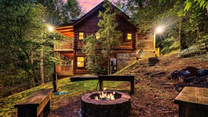Eine Blockhütte mit Feuerstelle, einer Holzterrasse und einer Treppe, die zu einem Balkon führt.