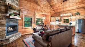 Ein Holzblockhaus-Interieur mit Kamin, Ledersofa, Essbereich und Küche.