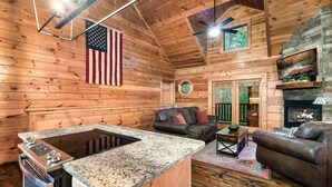 Ein Holzblockhaus-Interieur mit Kücheninsel, Kamin, einer Couch und einem Fernseher.